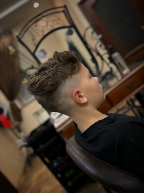 На фото представлена современная модельная стрижка для мальчика, сочетающая элементы фейда и текстурированного верха. 01
