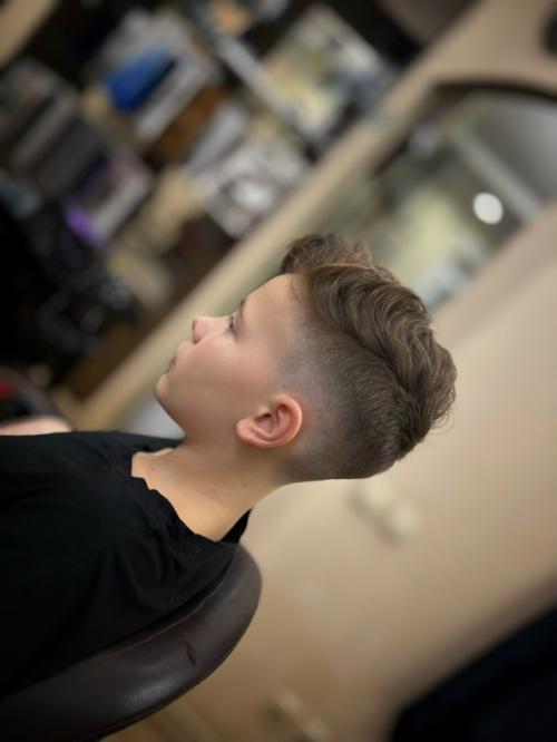 На фото представлена современная модельная стрижка для мальчика, сочетающая элементы фейда и текстурированного верха. 02